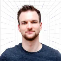 Portrait of a man with short brown hair and a trimmed beard, wearing a dark blue shirt, facing the camera in a white grid backdrop.